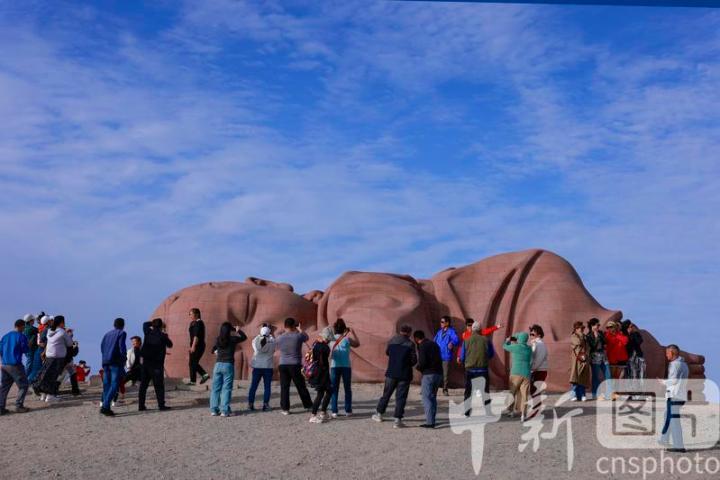 2024年9月19日，位于甘肃省酒泉市瓜州县城南20公里的戈壁国际雕塑艺术长廊，游客在雕塑艺术作品《大地之子》前打卡拍照。中新社发　陈坤　摄