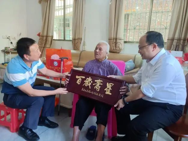 ▲镇党委副书记、镇长吴江龙（右一）向新晋百岁老人敬赠“百岁寿星”牌匾。