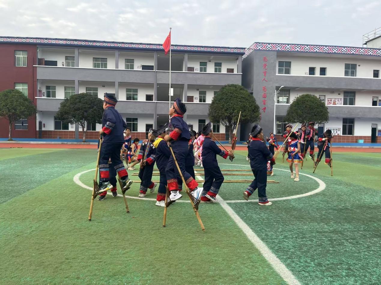 图说：学生们身着民族服装练习踩高脚、跳竹竿舞、吹芦笙。