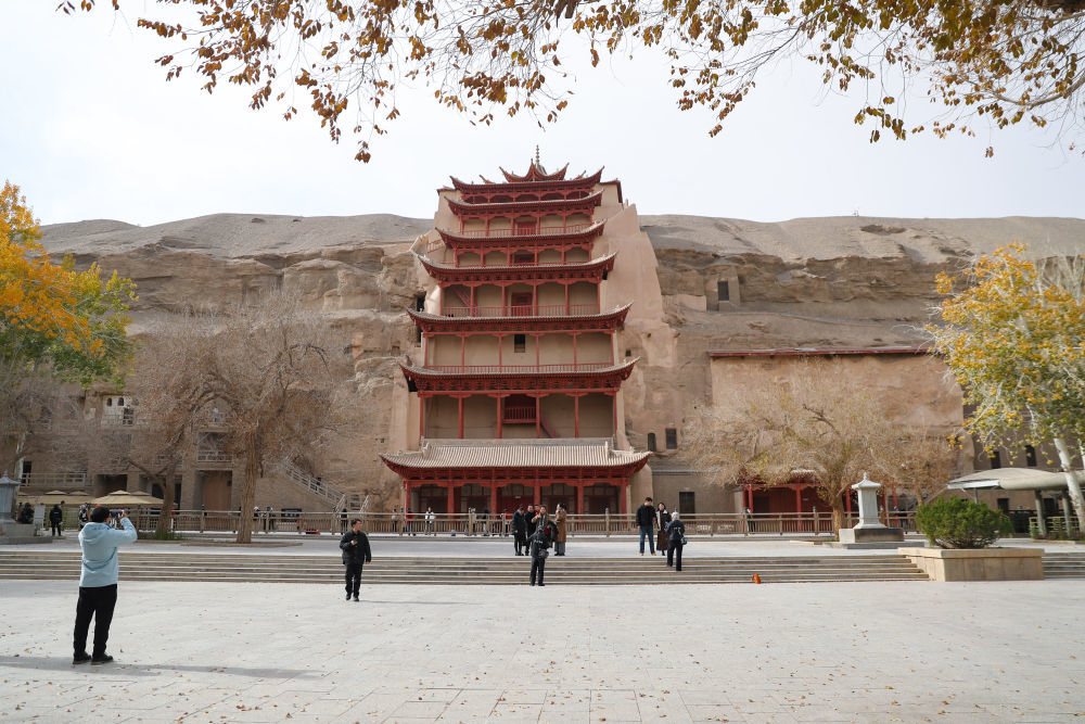 ↑11月14日，游客在莫高窟标志性建筑九层楼前拍照留念。