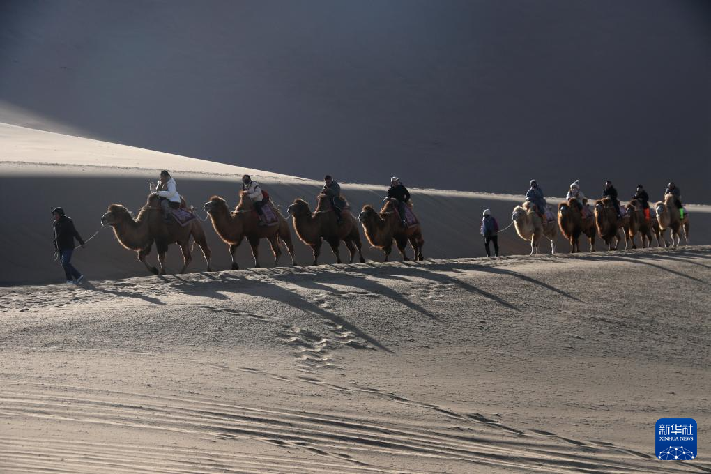 12月1日，游客在甘肃省敦煌市鸣沙山月牙泉景区骑骆驼游览。