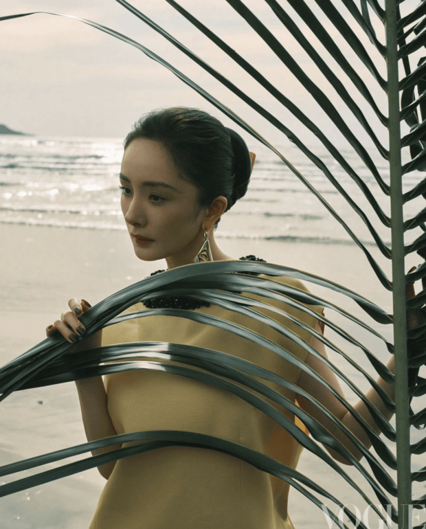 杨幂手持棕榈叶轻遮身侧，暖调造型衬得气色柔和。