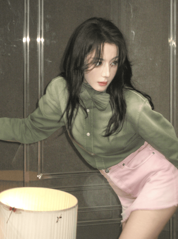 迪丽热巴穿绿调上衣搭配粉色短裙，姿态随性舒展。