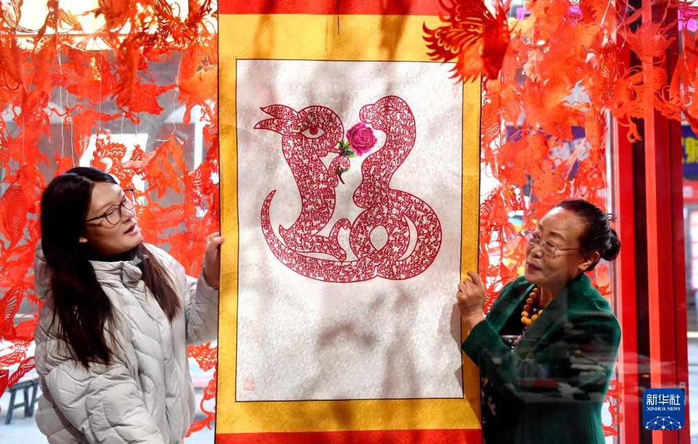 1月3日,蔚县剪纸国家级代表性传承人周淑英(右)在河北省石家庄市新华区名家工作室向剪纸爱好者介绍生肖蛇作品。