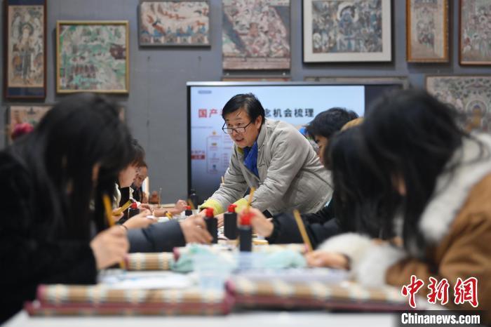 1月14日，甘肃省酒泉市，甘肃酒泉职业技术学院非物质文化遗产敦煌彩塑技艺传习所内，该校甘肃省级敦煌壁画技艺传承创新工作室负责人王权朝向学生们教授敦煌文创创作方法。中新社记者　李亚龙　摄