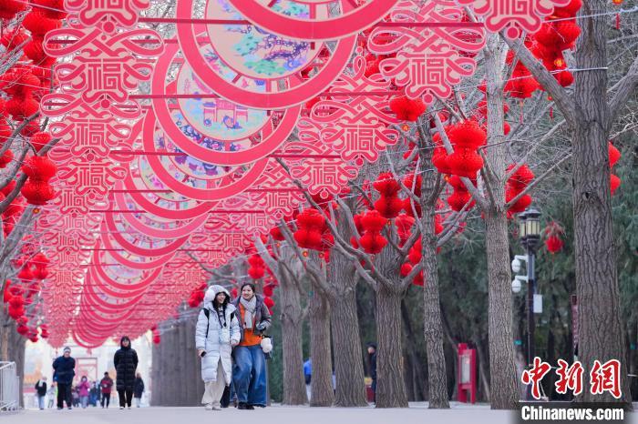 1月17日，地坛公园张灯结彩，市民从春节装饰下经过。近日，北京地坛公园进行庙会景观布置，大红灯笼将公园装点得年味十足。　中新社记者 赵文宇 摄