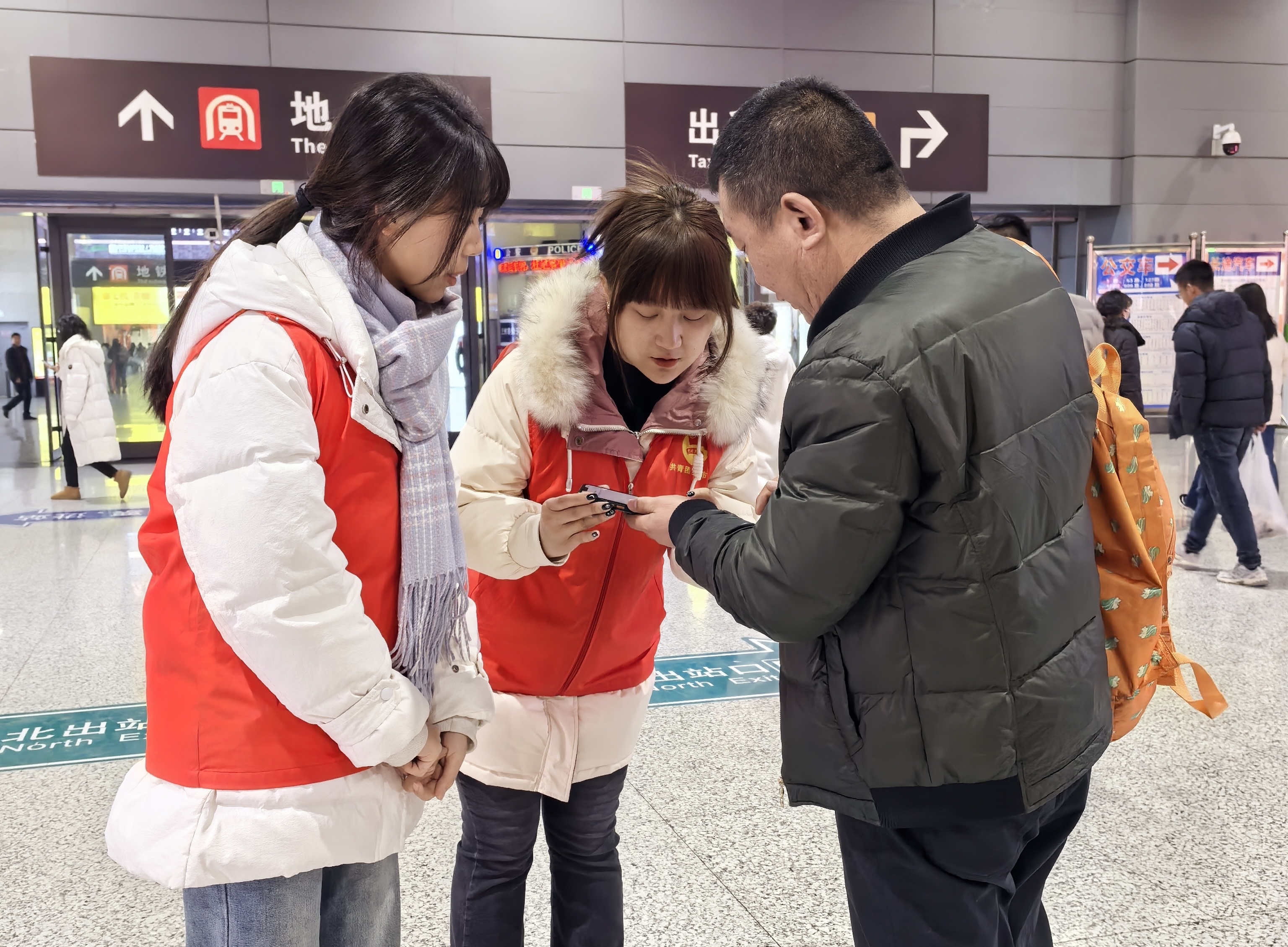 大学生志愿者帮助旅客在手机上购买地铁票