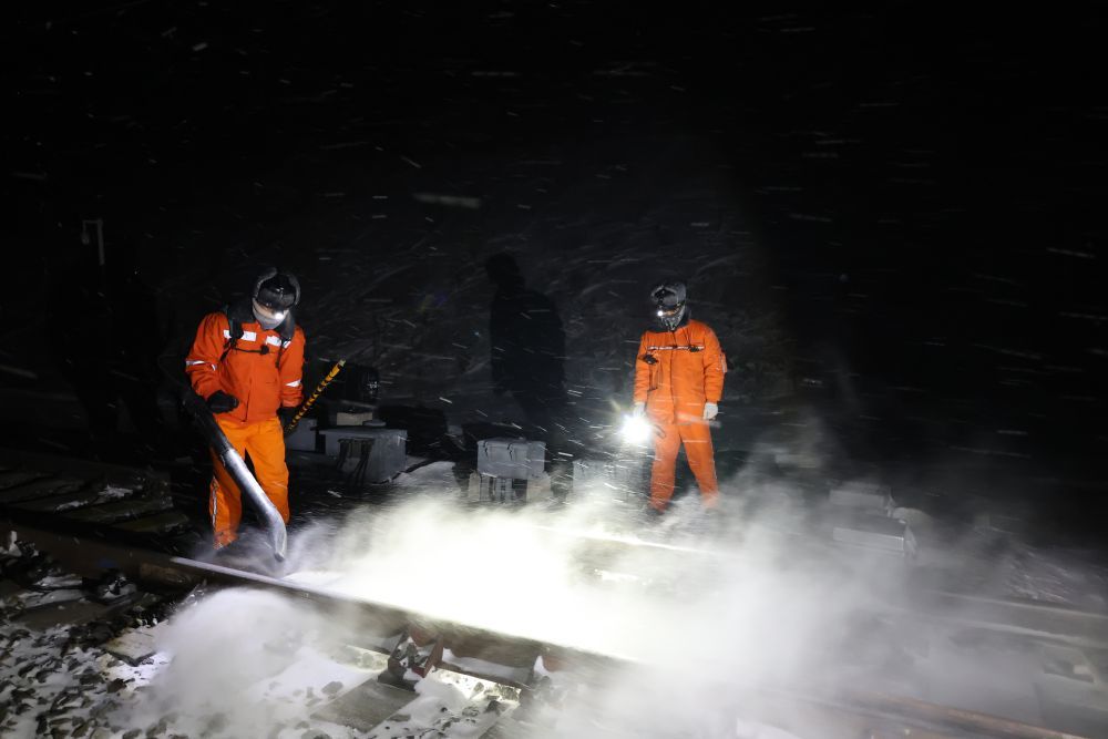 1月23日凌晨，新疆铁路乌鲁木齐供电段苏布台值守点的职工郑金刚（右）和陈勇贵利用列车经过间歇清理铁轨道岔中的积雪。新华社记者　张啸诚　摄