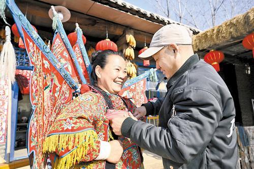 1月21日，甄淑梭（左）在丈夫马三权的帮助下，穿上十多斤重的戏服准备开始直播。