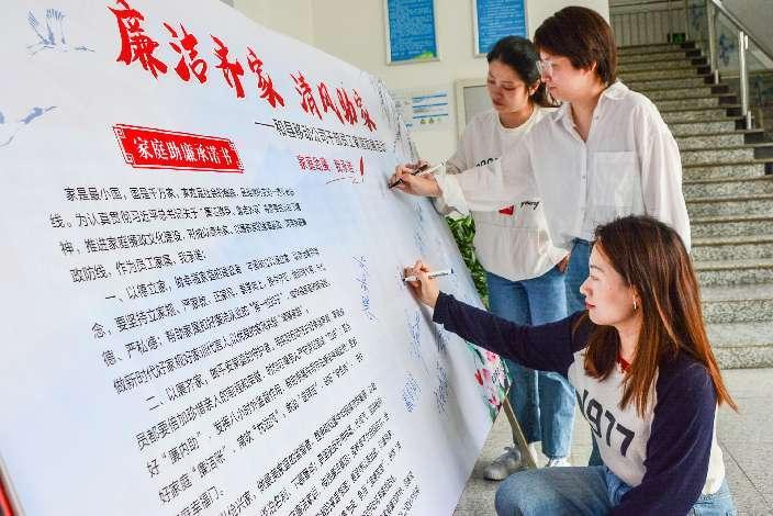 图为员工家属在家庭助廉承诺书上集体签名场景。