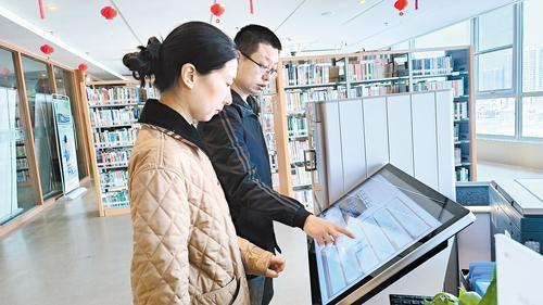 3月13日,廊坊市安次区图书馆服务台前,工作人员(右)正在指导读者用AI视觉盘点系统查询图书的具体位置。本报记者 刘英摄