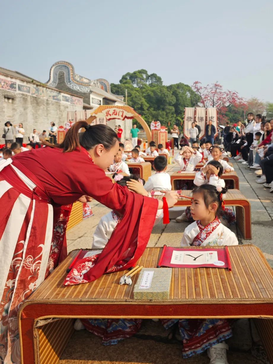 图：现场，园长、老师在学童的额头正中点上朱砂，寓意学生从此开启智慧，目明心亮