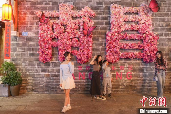 4月5日，江西南昌万寿宫历史文化街区，游客在由花朵组成的“南昌”二字前拍照“打卡”。当日正值清明假期，众多游客夜游万寿宫历史文化街区，享受美好假日时光。中新社记者 刘力鑫 摄
