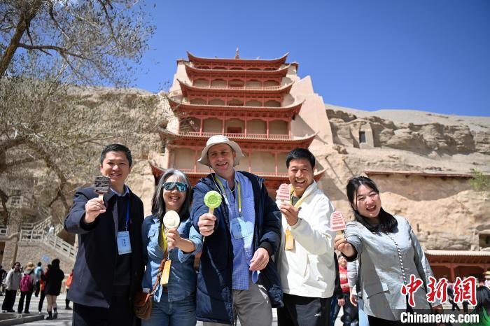4月11日,甘肃敦煌,中外嘉宾在莫高窟标志性建筑九层楼前,手持文创雪糕合影留念。九美旦增 摄