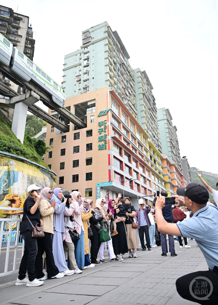 境外旅行团正在李子坝观景平台打卡轨道列车穿楼。