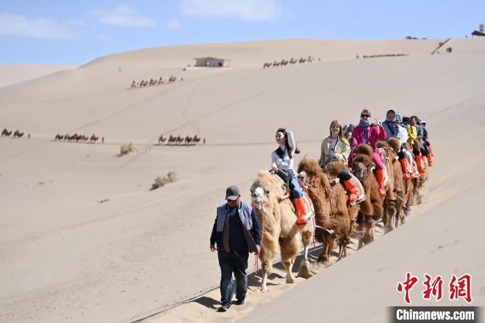 4月11日,甘肃敦煌,中外嘉宾在鸣沙山体验骑骆驼。九美旦增 摄