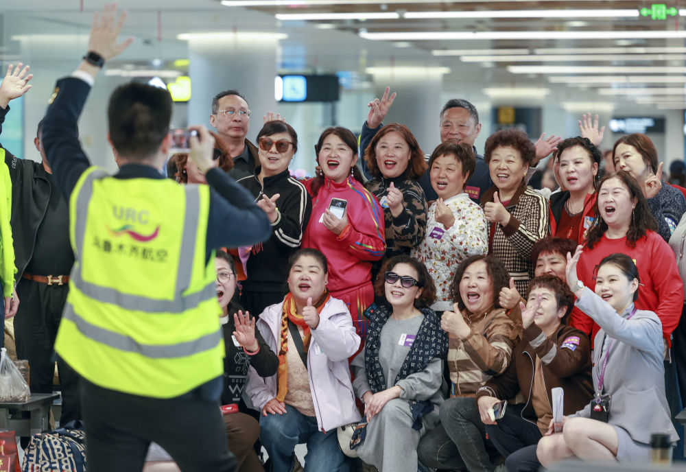 4月17日，旅客在乌鲁木齐天山国际机场北区航站楼候机厅与乌鲁木齐航空公司工作人员合影留念。新华社记者 王菲 摄