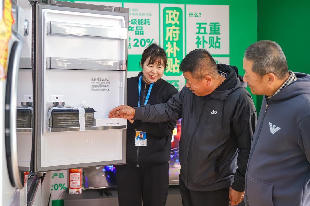 青岛市李沧区九水街道侯家庄社区国补换新服务站，工作人员向居民介绍家电产品和补贴政策。