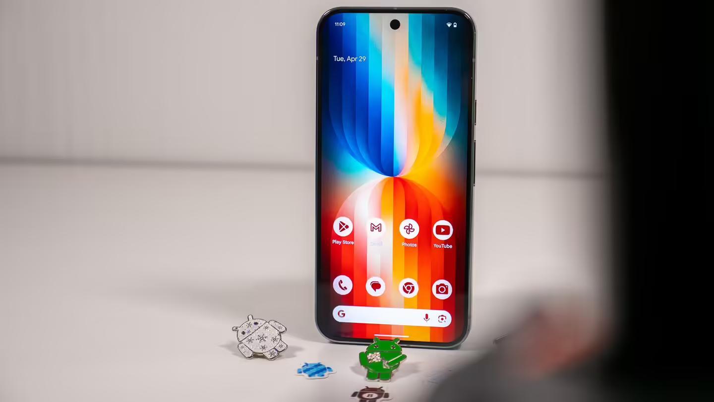 A Google Pixel 9 Pro XL with a red and blue wallpaper from the App Backdrops, including Android pins and stickers in front of the phone