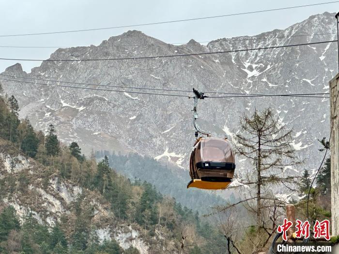 图为缆车试运行，背后是皑皑雪山。官鹅沟由官珠沟、鹅嫚沟、雷古山等核心游览区组成，2022年被确定为国家5A级旅游景区。据了解，“五一”假期期间，雷古山索道往返票价享五折优惠。闫姣　摄