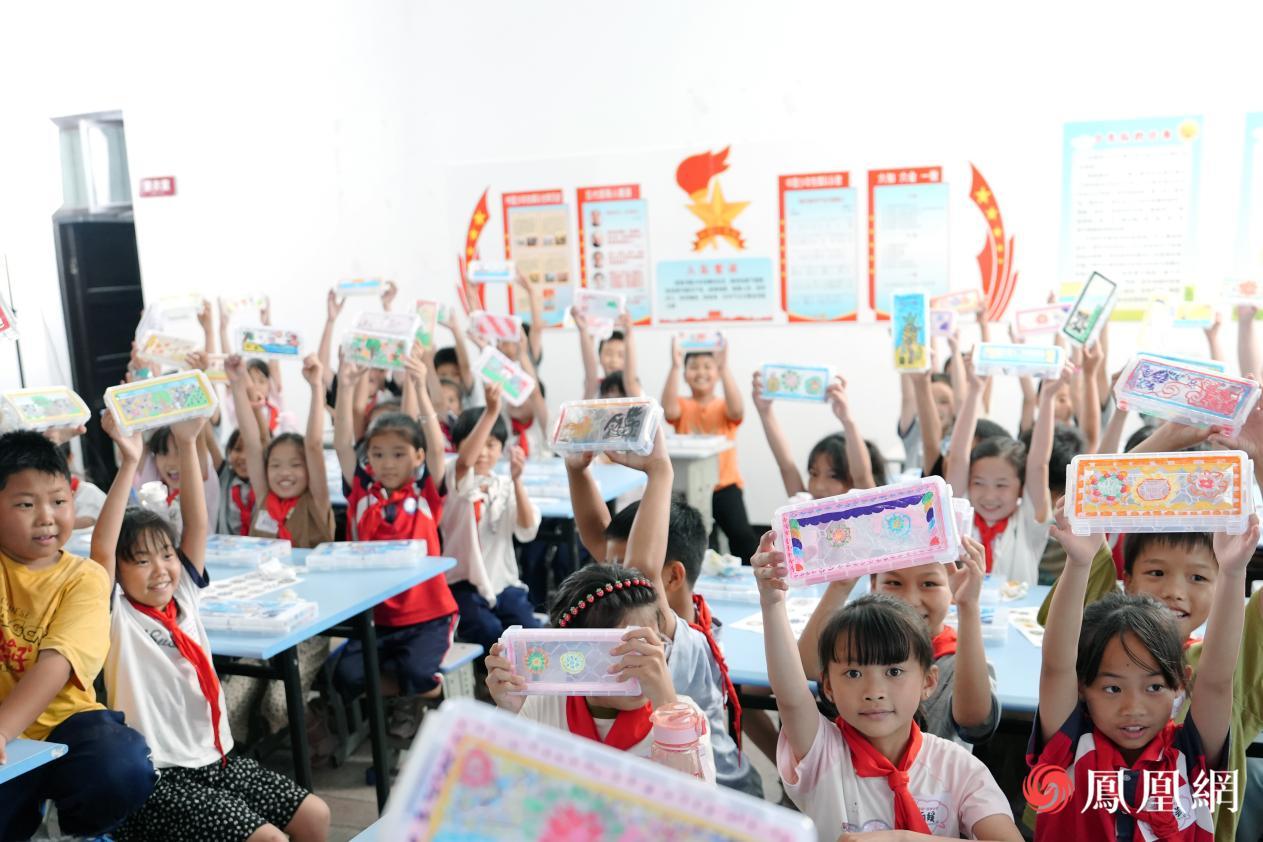 孩子们高举绘制的笔盒向镜头展示，稚嫩脸庞洋溢着满满的成就感