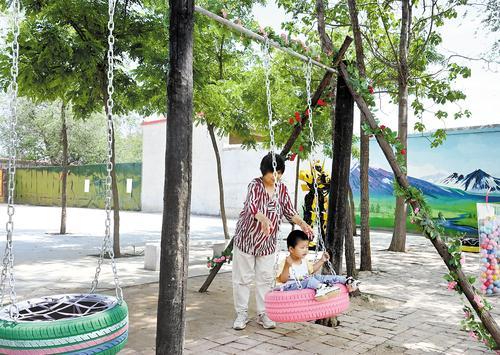 5月17日，在威县马家庄村广场上，一位村民带着孙子在废轮胎制作的秋千上玩耍。 本报记者 吕若汐摄