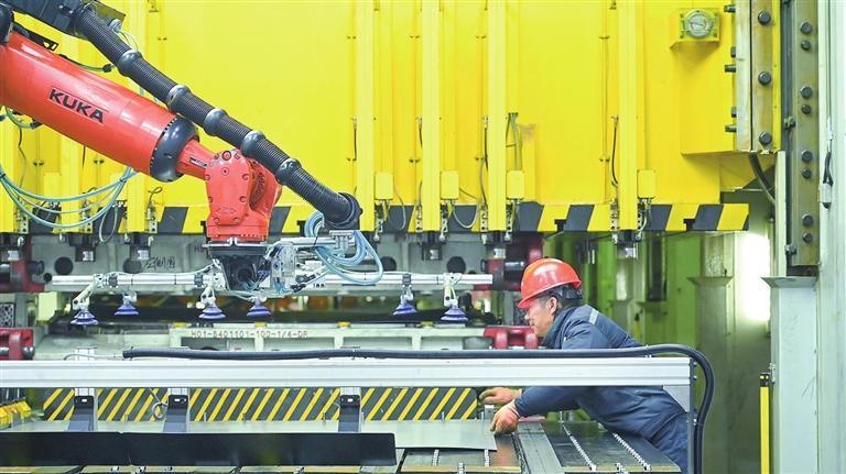 知豆冲压车间内，工人辅助智能机械臂运送金属板。