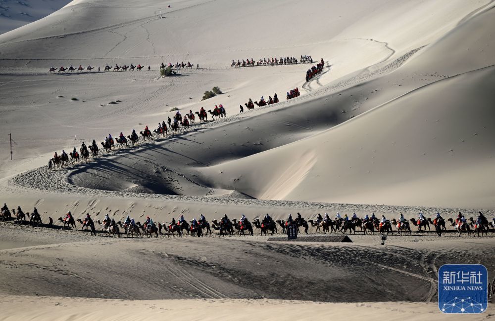 5月24日，游客骑骆驼在甘肃省敦煌市鸣沙山月牙泉景区游览。
