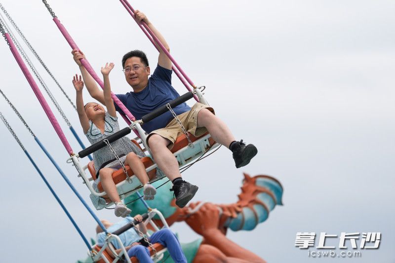 一对父子在咸嘉湖沙滩游乐园旋转飞椅上欢快玩耍。均为长沙晚报全媒体记者 郭雨滴 摄