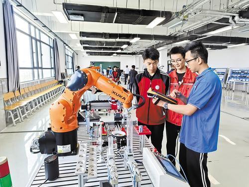 5月27日，2022级中德2班学生李景扬（右）向师弟们展示毕业设计——新能源电池智能装配工作站。 本报记者 解楚楚摄