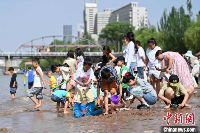 5月31日，甘肃兰州，小朋友在黄河岸边戏水游玩。端午假期首日，众多游客选择在黄河兰州段的茶摊喝茶，乘坐羊皮筏子、快艇游览黄河。中新社记者　九美旦增　摄
