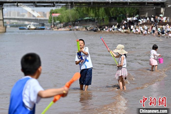 5月31日，甘肃兰州，小朋友在黄河岸边戏水游玩。端午假期首日，众多游客选择在黄河兰州段的茶摊喝茶，乘坐羊皮筏子、快艇游览黄河。中新社记者　九美旦增　摄