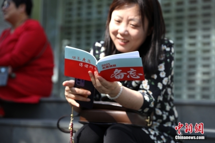 6月7日，2025年全國高考拉開帷幕。位于北京的中國人民大學附屬中學考點外，家長翻閱2025志愿填報備忘資料。中新社記者 趙雋 攝