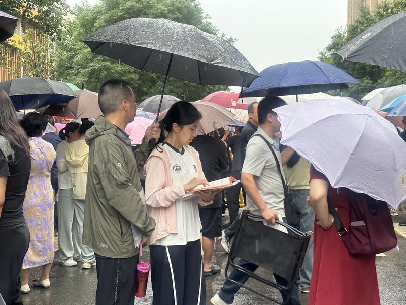 在西安市高新第二初级中学考点，家长为孩子撑起雨伞，考生抓住最后的时间复习要点（记者 程静摄）