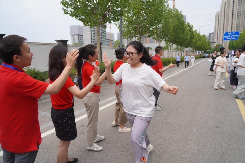 西安市高新第一学校考点外，身着红色衣服的老师与考生们击掌，成为考场外动人的 “加油风景” 。（记者 程静摄）