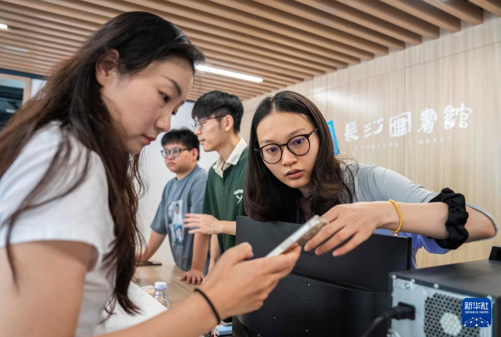 6月28日,在长沙图书馆湘江新区周家湾分馆,工作人员(右一)为市民答疑。
