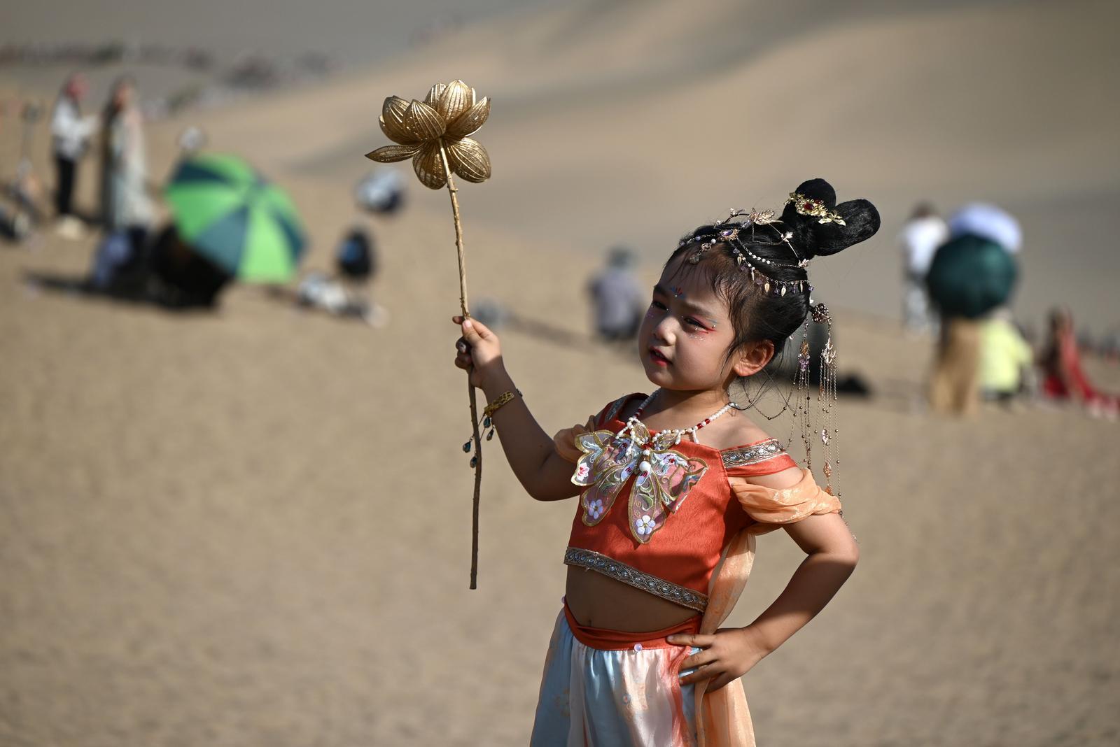 2025年7月26日，身着“飞天”服饰的小朋友在甘肃省敦煌市鸣沙山月牙泉景区拍照。