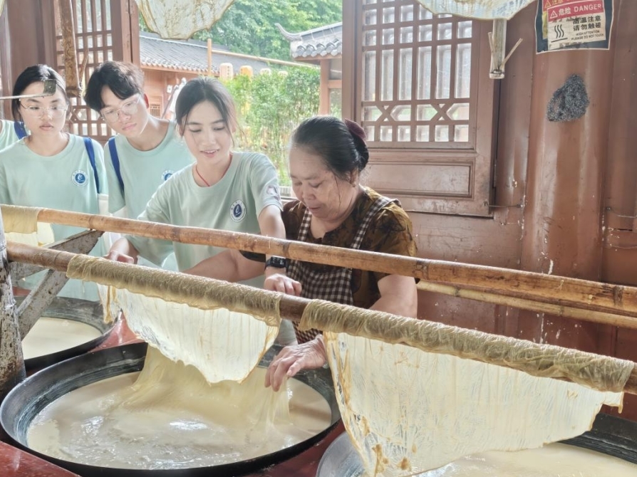队员们在老手艺人的指导下学习制作腐竹。