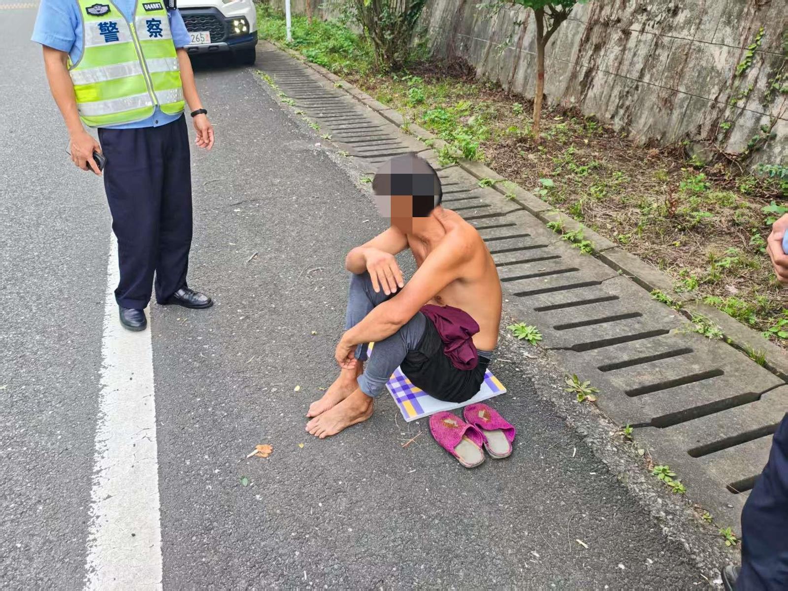 男子赤裸上身坐在高速公路应急车道行道树下