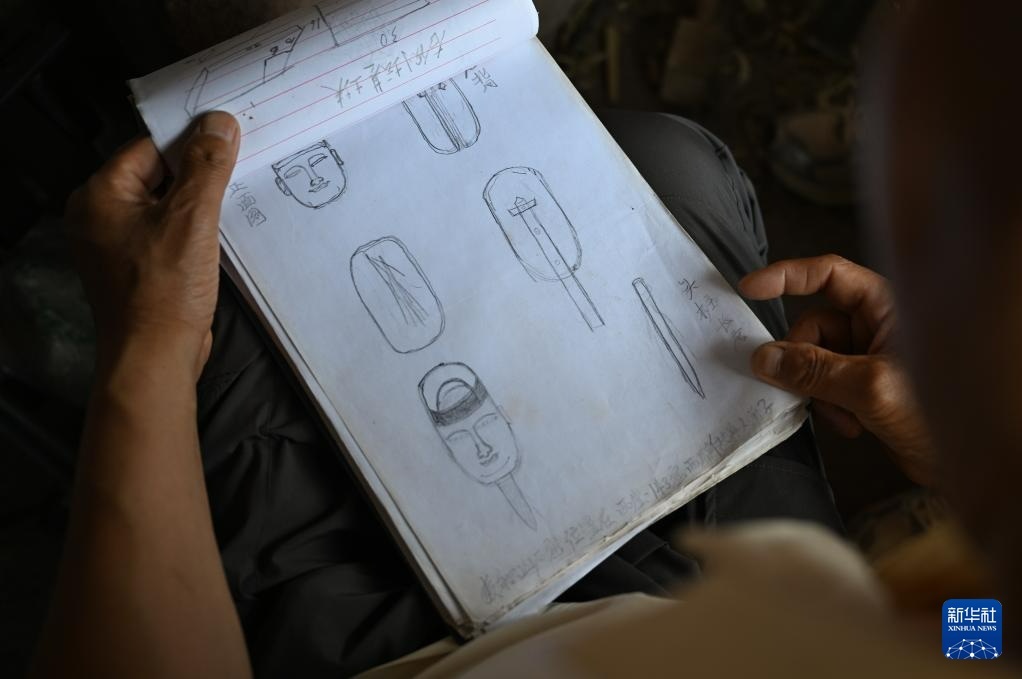 牟常有在麦积山石窟翻看自己绘制的修复草稿图（7月16日摄）新华社记者　蔡湘鑫　摄