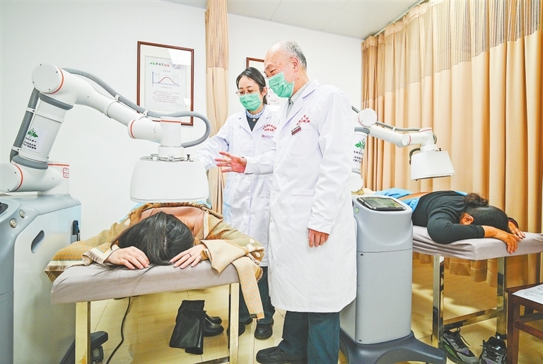 3月6日,在江西中医药大学附属医院西湖院区,热敏炙创始人陈日新(右)教授利用热敏炙机器人进行临床治疗。