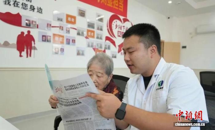 正在陪老人看報紙的李睿。　李天鵬 攝