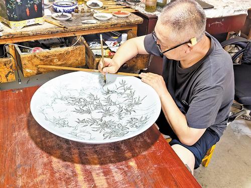 8月22日，在望月轩陶瓷工坊，工人正在描画九桃大盘。本报记者 刘 杰摄