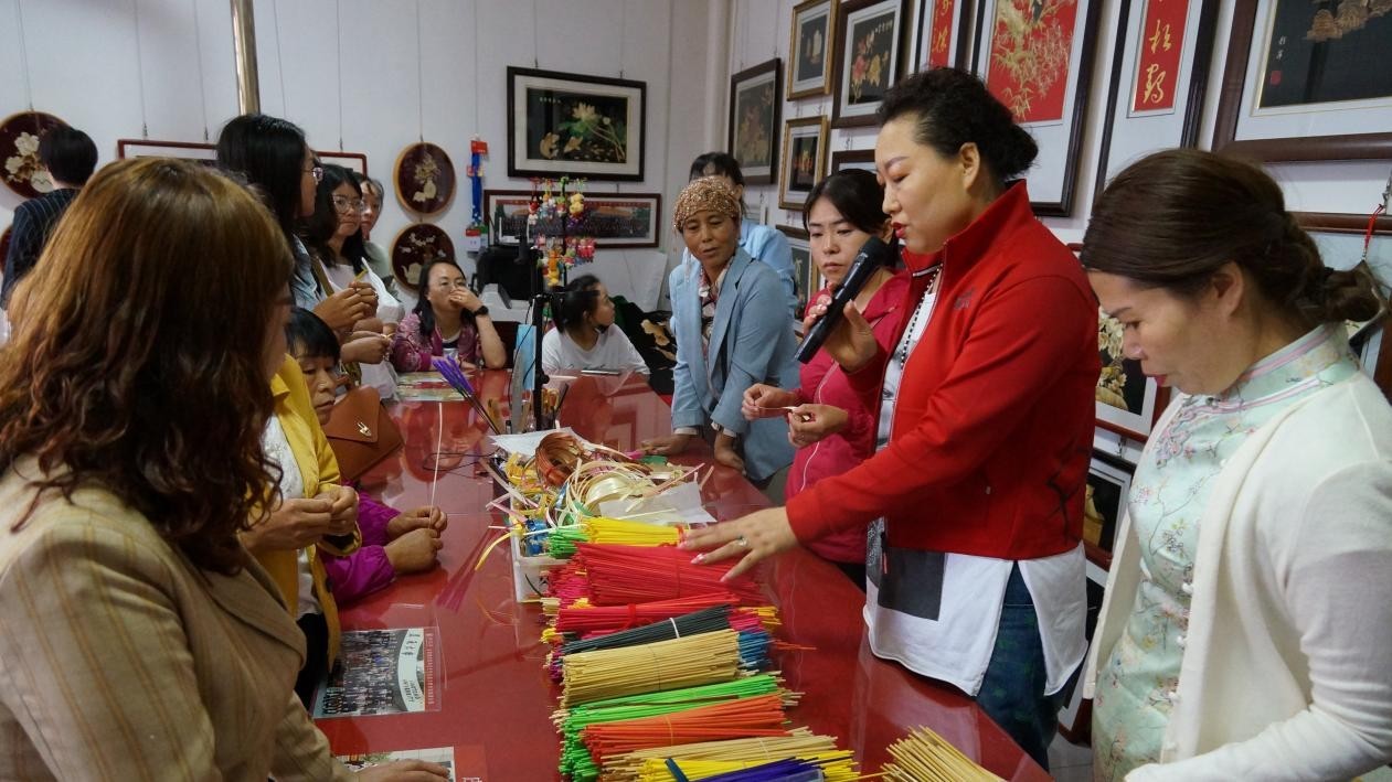 （唐彩萍在扶贫车间为留守妇女讲解麦秆画的制作方法）