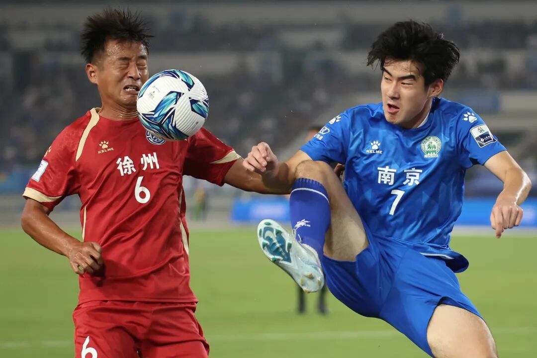🔹9月6日晚，2025年江苏省城市足球联赛（苏超）迎来第十一轮燃情对决，图为南京队球员（蓝）与徐州队球员在比赛中拼抢。中新社记者 泱波 摄
