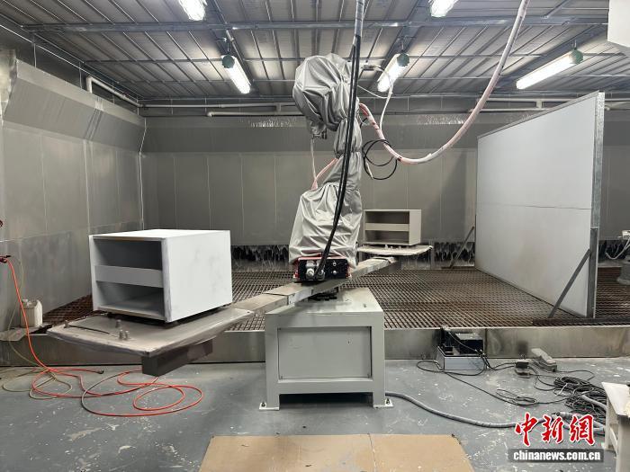 图为16日，位于江西省赣州市南康区一公司生产车间内，机械臂不停挥舞转动，喷枪内的水性漆正对家具进行上色。朱莹 摄