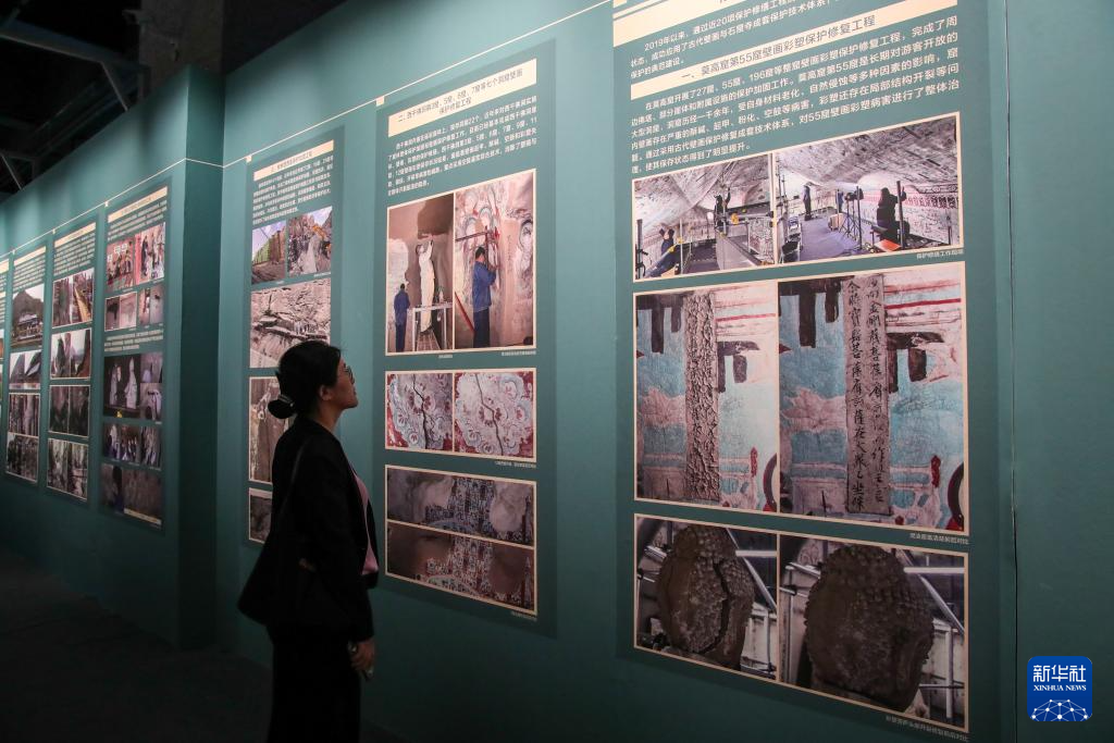 9月22日，在敦煌研究院“典范”“高地”建设成果展上，一名嘉宾在观看莫高窟壁画彩塑保护修复工程简介。