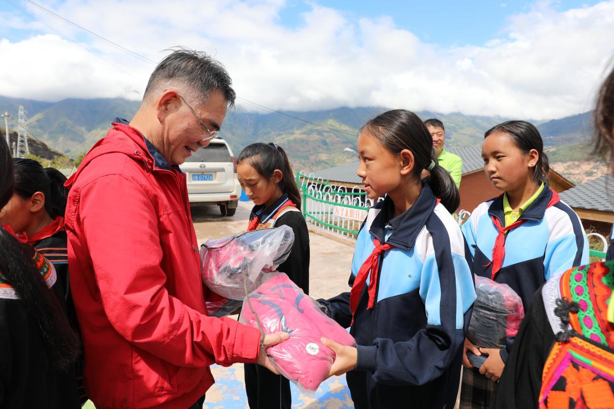 北仑区慈善总会会长张如平（左一）正为美姑县荞麦花开儿童之家的学生发放运动服