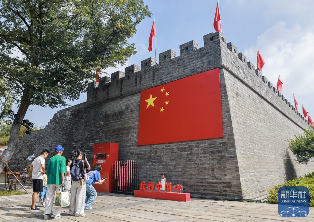 ↑ 10月1日,在浙江嘉兴市南湖区建设街道子城城墙边,市民与国旗合影。新华社记者 徐昱 摄
