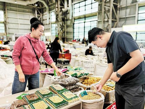 9月27日,在安国市数字中药都中药材交易市场一号馆,中药材经营户(左)在为采购商介绍中药材。 保定市行政审批局供图